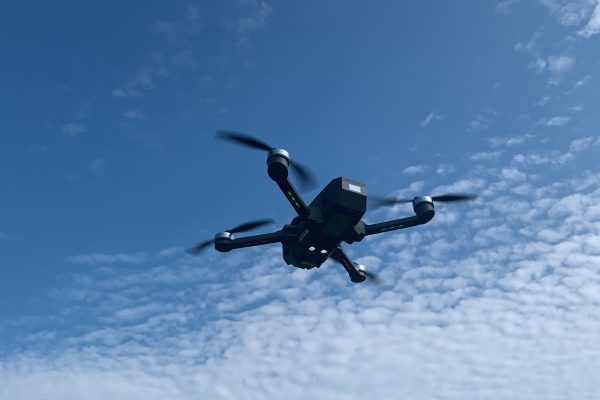 Dron cuadricóptero con cámara visto desde abajo mientras vuela en un cielo azul con nubes