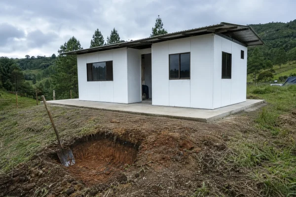 Casa prefabricada sobre placa de concreto y apique abierto junto a ella en un lote de ladera