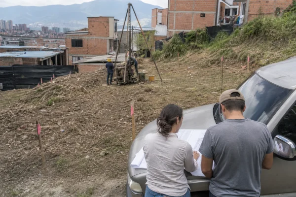Sondeo geotécnico en un lote mientras el arquitecto y el dueño revisan los planos