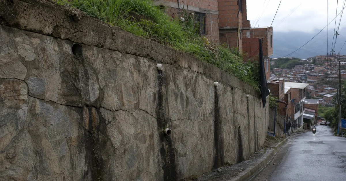 Muro de contención de piedra inclinado y agrietado en una calle de ladera de Medellín