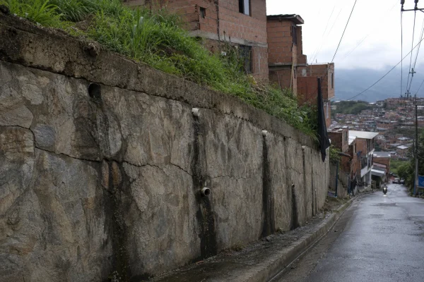 Muro de contención de piedra inclinado y agrietado en una calle de ladera de Medellín